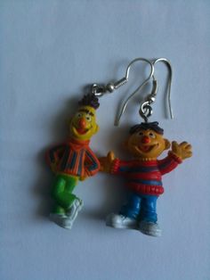 two toy figures are hanging from silver earwires