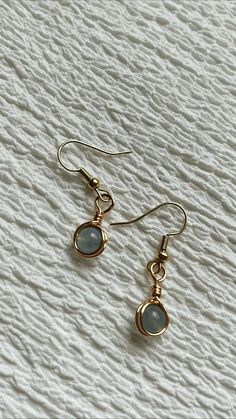 the gold earrings are hanging from the hooks on the white fabric background, with small blue stones embedded in them