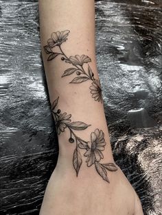 a woman's hand with a tattoo on the wrist and flowers growing out of it