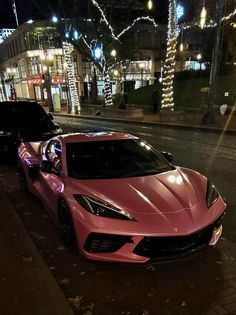 two pink sports cars parked on the side of the road at night with christmas lights in the background