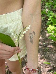 a woman holding a flower in her right hand with a small tattoo on it's arm