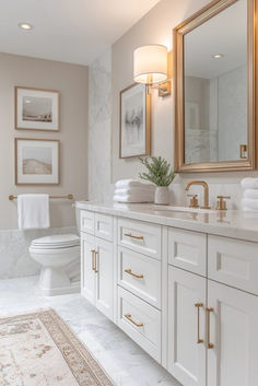 a white bathroom with gold accents and marble counter tops, along with a large mirror on the wall