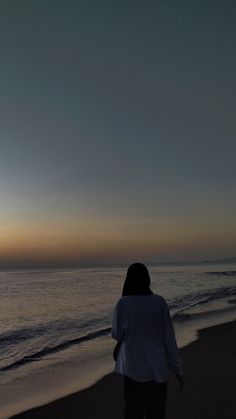 a person standing on the beach watching the sun go down over the ocean and water