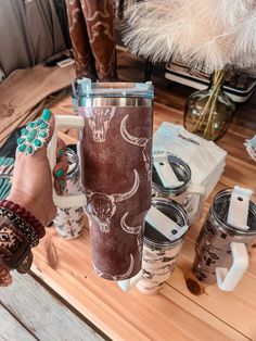 a person holding a coffee cup on top of a wooden table next to other items