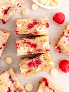 raspberry cheesecake bars cut into squares on a marble surface with white chocolate chips and raspberries