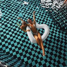 two women in bikinis floating on an inflatable pool with checkered flooring