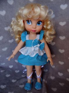 a doll with blonde hair wearing a blue dress and white polka dot shoes on a gray background