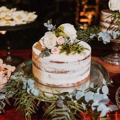 a wedding cake with flowers on top and greenery around the edges is sitting on a table