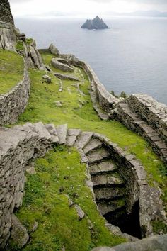 an old stone wall with stairs leading to the water and grass growing on it's sides