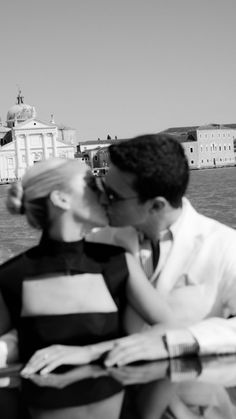 a man and woman kissing while sitting next to each other on a bench near the water