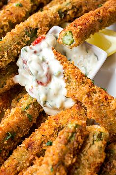 some fried food on a white plate with sauce and lemon wedges next to it