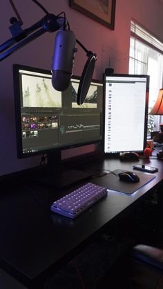 a desk with two computer monitors and a keyboard on it, in front of a lamp