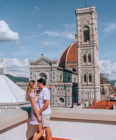 a man and woman standing on top of a roof next to each other in front of a cathedral