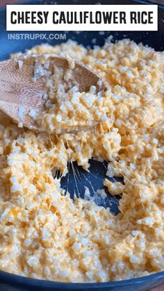 cheesey cauliflower rice in a blue bowl with a wooden spoon on top