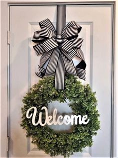 a wreath with the word welcome hanging on it's front door is decorated with black and white ribbon