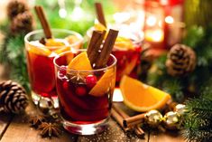 two glasses filled with mulled and orange slices on a wooden table next to pine cones