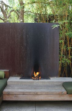 a fire pit in the middle of a patio with green cushions and bamboo trees behind it