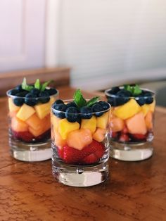 three small glasses filled with fruit on top of a wooden table