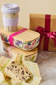 two wrapped gifts sitting next to each other on a table with a coffee cup and paper wrapper