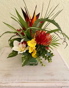 a vase filled with lots of flowers on top of a white wooden table next to a wall