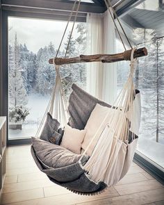 a hammock chair hanging in front of a window with snow covered trees outside