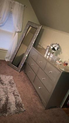 a bedroom with a dresser, mirror and window in the corner next to a rug on the floor