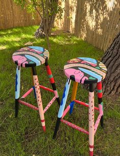 two children's stools sitting in the grass next to a tree and fence