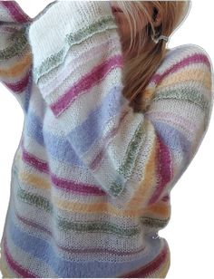 a woman wearing a multicolored sweater with her hands behind her head and looking down at the ground