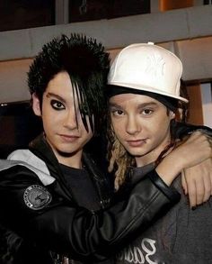 two young men are hugging each other in front of a building and one is wearing a white hat