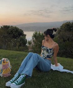 a woman sitting on the grass next to a blanket