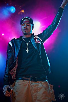 a man standing on stage with his arms in the air while wearing a leather jacket