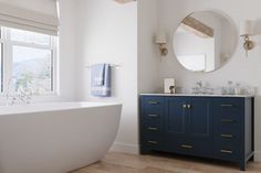 a white bath tub sitting next to a bathroom sink under a round mirror on top of a wooden floor