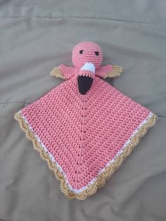 a pink crocheted blanket with a stuffed bird on it's back, sitting on a bed