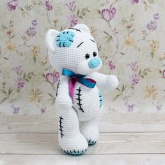 a crocheted white teddy bear with blue eyes and pink bow on it's neck