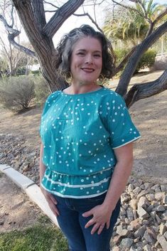 a woman standing in front of a tree with her hands on her hips and smiling