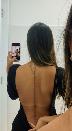 a woman taking a selfie with her cell phone in front of her back tattoo