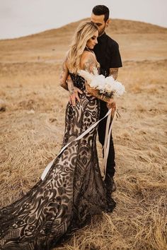 a man standing next to a woman in a dress on top of a dry grass field