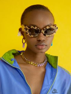 a woman wearing sunglasses and a blue shirt with leopard print on the front, standing in front of a yellow background