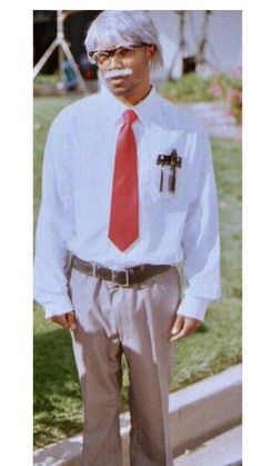 an older man wearing a white shirt and red tie standing in front of some grass