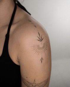 a woman's arm with an arrow and sunburst tattoo on her left shoulder