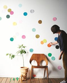 a woman standing next to a chair in front of a wall with colorful circles on it