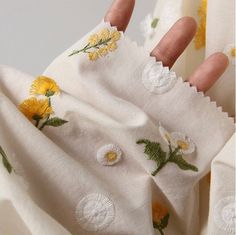 a person's hand holding onto some white fabric with yellow flowers on it