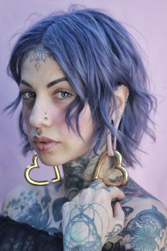 a woman with blue hair and piercings on her face is posing for the camera