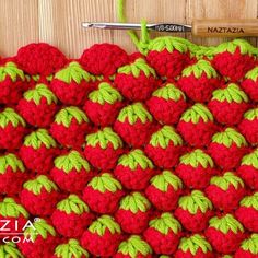 a crocheted red and green wall hanging on a wooden wall with a ruler next to it