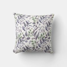 a white pillow with purple and green leaves on the front, sitting against a wall