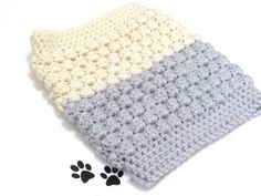 a gray and white crocheted blanket with paw prints on the floor next to it