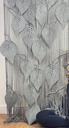 a woman sitting on the floor in front of a wall hanging made out of yarn