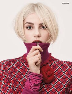 a woman with short blonde hair wearing a red sweater and holding a flower in her mouth