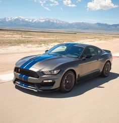 a silver car driving down a race track with mountains in the backgrouund