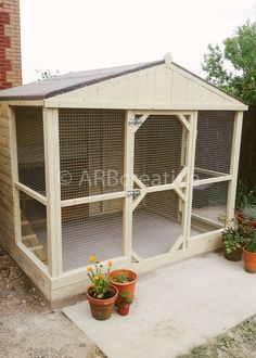 an outdoor chicken coop with plants and potted flowers on the ground in front of it